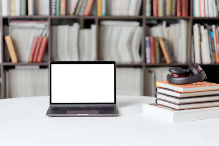 A stack of books with headphones on the background of a rack of books in the reading room of the library. Student poster.の写真素材