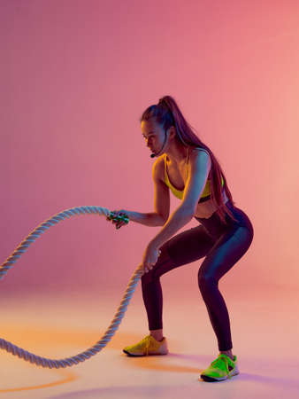 Athletic cool girl trainer teaches group crossfit and work out online training on a bright neon background.の写真素材