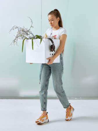 A pretty young girl walks with office supplies in a box, sad, after being cut and fired at work due...