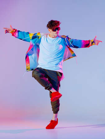 Guy dancing contemporary dance in studio. Neon light grey background. Acrobatic bboy dancer. Break dance lessons.の写真素材