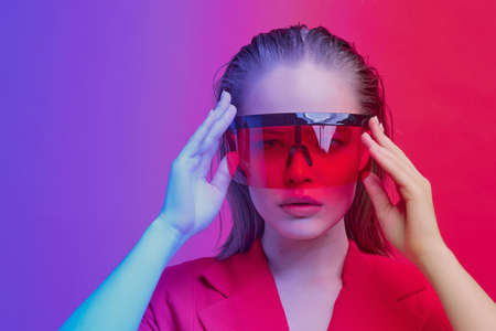 Cool stylish girl with a fashionable hairstyle and stylish glasses with a large glass poses on a bright neon background.の写真素材