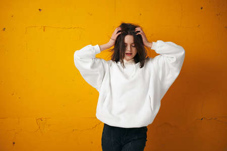 Portrait of a young pretty female student in a white hoodie, casual clothing against a concrete orange wall.の写真素材