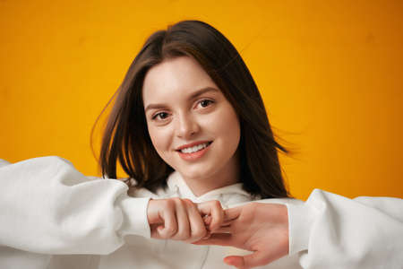 Portrait of a young pretty female student in a white hoodie, casual clothing against a concrete orange wall.の写真素材