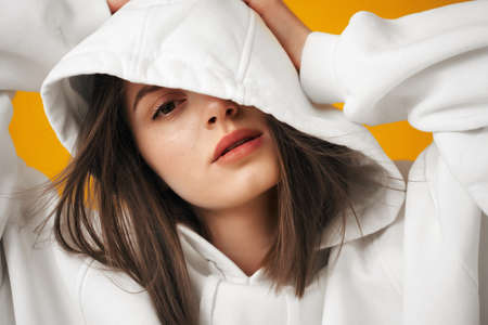 Portrait of a young pretty female student in a white hoodie, casual clothing against a concrete orange wall.の写真素材