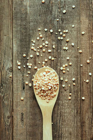 Dried pea fruits are placed in a wooden spoon on an aged wooden table, a poster of vegan food.の写真素材