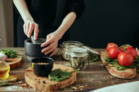A young pretty girl grinds spices in a mortar while cooking a dish, fresh ingredients are spread out on a wooden table.の写真素材