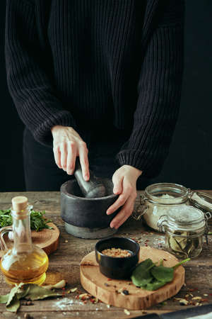 A young pretty girl grinds spices in a mortar while cooking a dish, fresh ingredients are spread out...