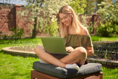 Creative young girl blogger working on a laptop on content sitting in the backyard of a house in the garden on a lawn.の写真素材