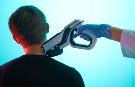 Doctor in uniform gives a chip injection with modern syringe to a young man in the neck, chipization of the population.の写真素材