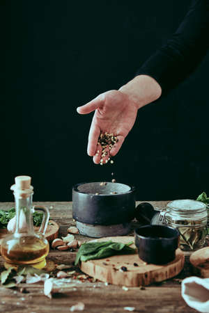 A mans hand pours pepper and spices into a mortar for grinding when cooking. Cooks poster still life.の写真素材