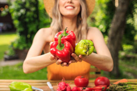 Young pretty girl in a hat is sitting at wooden table with fresh vegetables grown in her garden in...