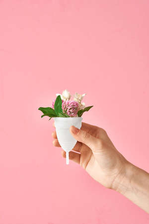 Eco friendly soft white silicone menstrual cup with flowers in girls hand isolated on pink backgroundの写真素材