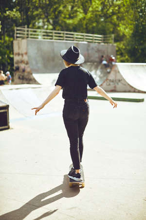 Young teenage girl in hat rides a skateboard in a skatepark in a black clothes, active and sport...