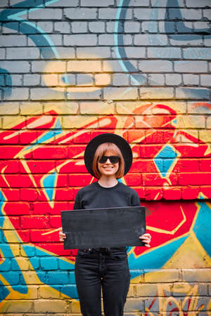 Young girl with cardboard sign of protest in hat and sunglasses stand against brick wall with...