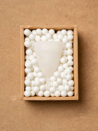 Menstrual cup eco friendly reusable and silicone in in a craft box in white balls isolated on beige...