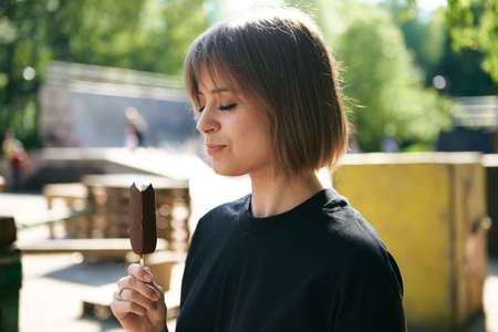 Pretty young girl enjoys eating ice cream in park, cozy photography for blog or advertising, happy lifestyleの写真素材