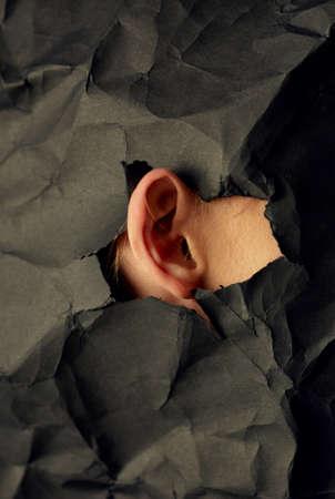 Womans ear in hole in black crumpled paper background, black and white concept photography for blog or posterの写真素材