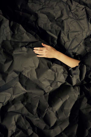 Womans hand comes out of hole in black crumpled paper background, a concept photography for beauty...