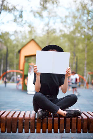 A young cute modern millennial hipster girl in a hat dressed in black is relaxing reading book in a city Park.. High quality photoの写真素材