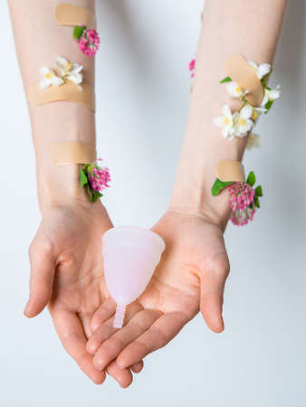 Eco-friendly soft white silicone menstrual cup in girls arms decorated with flowers isolated on white backgroundの写真素材