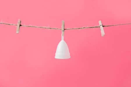 Menstrual cup white eco friendly hanging on clothesline isolated on pink background, photo for womens blog or ad posterの写真素材