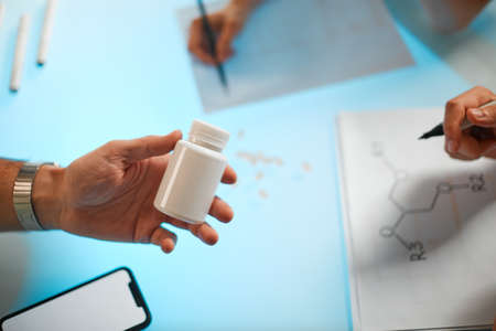 White jar of fish oil capsules in the hand of a scientist. Close up photography for ad or healthy lifestyle blog. High quality photoの写真素材