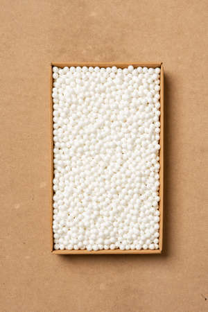 Cardboard box with white packing foam pellets, white polystyrene foam on a beige backgroundの写真素材