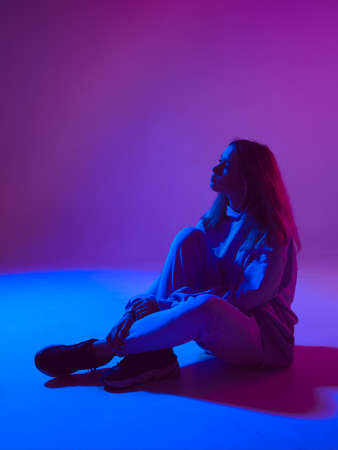 Stylish young girl, cool posing in a hoodie on the floor on a neon background. Dance school posterの写真素材