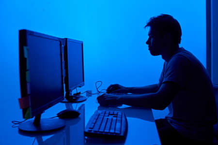 Hacker tries to break security system to steal important company information, working at laptop in blue neon lightの写真素材