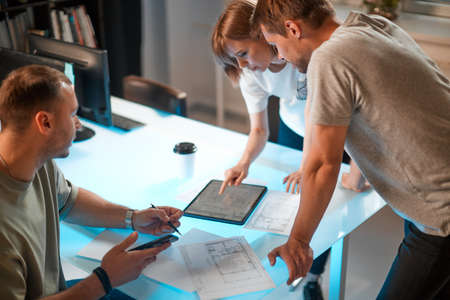 Creative team of architects designers discussing ideas, working with tablet in modern office