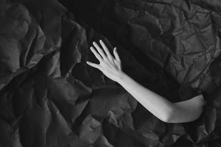 Womans hand comes out of hole in black crumpled paper, black and white concept photography for...