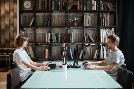 Young designers girl and guy work at computers in office on the background of the library