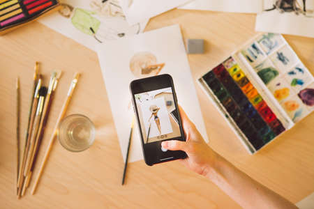 Illustrator girl blogger takes picture of  drawing on phone. Photography for ad courses illustrations or blogの写真素材