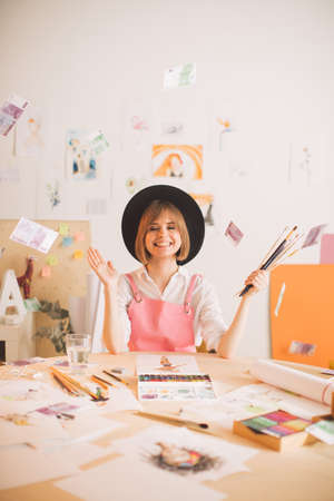 Creative smiling girl illustrator sitting under rain of money in workshop. Concept photo about art and freelanceの写真素材