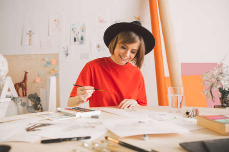 Young pretty teen girl artist in hat draws watercolors in studio. Photo for advertising courses illustrations or blogの写真素材