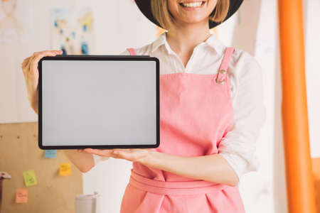 Close up of smiling pretty woman artist showing blank screen tablet. Cozy photography for ad or blogの写真素材