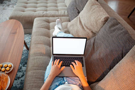 Teen girl lying on sofa with blank screen laptop watching series at cozy atmosphere. Close up photography for ad or blogの写真素材