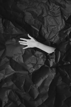Womans hand comes out of hole in black crumpled paper, black and white concept photography for beauty blog or posterの写真素材
