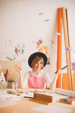 Creative smiling girl illustrator sitting under rain of money in workshop. Concept photo about art and freelanceの写真素材