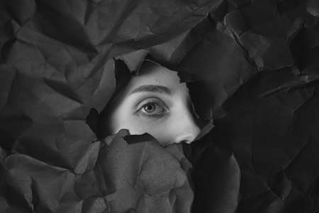 Womans closed eye in hole in black crumpled paper background, black and white concept photography...