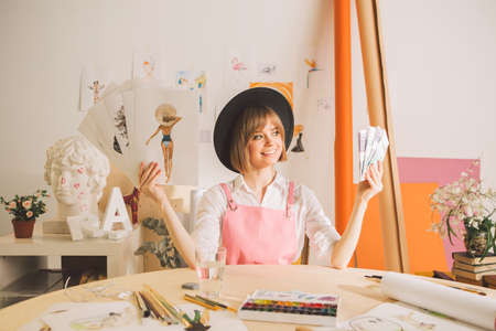 Creative girl artist or illustrator sitting with cash and brushes in workshop. Concept photo about art and freelanceの写真素材