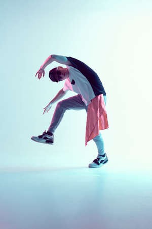 Guy dancing contemporary dance in studio. Neon light blue background. Acrobatic bboy dancer. Break...