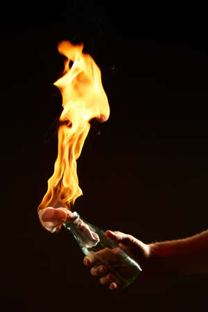 Males hand with a burning Molotov cocktail isolated on black background. Concept photography about protests and warの写真素材