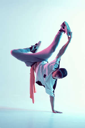 Young breakdancer guy stands on one hand dancing hip-hop in neon light. Dance school posterの写真素材