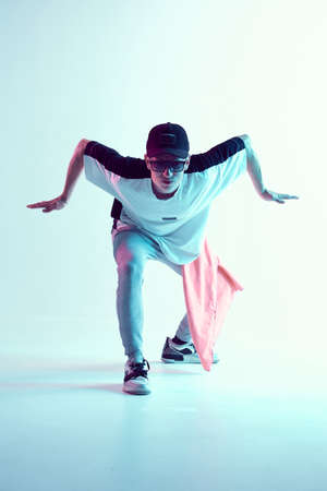 Guy dancing contemporary dance in studio. Neon light blue background. Acrobatic bboy dancer. Break...