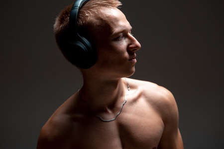 Cool young guy in wireless headphones listen to song with naked torso in studio. Music posterの写真素材