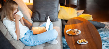 Teen girl sitting on sofa in Lotus position with blank screen laptop watching TV series. Close up photo for ad or blogの写真素材