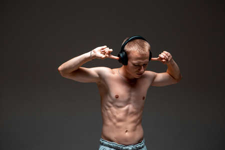 Cool young guy in wireless headphones with a naked torso listen to music in studio isolated on black backgroundの写真素材