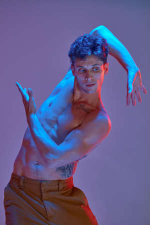 Cool young man dancing expressive dance without shirt in lilac neon light. Colorful dance school posterの写真素材