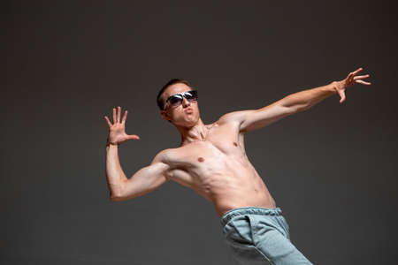 Cool young guy breakdancer in sunglasses dancing hip-hop without shirt in studio. Dance school posterの写真素材